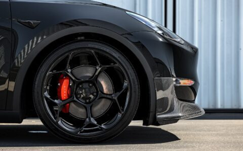 Detailed view of the Unplugged Performance front lip spoiler on a Tesla Model Y, showcasing the carbon fiber texture and precise fitment + the UP-05 forged wheel in gloss black.